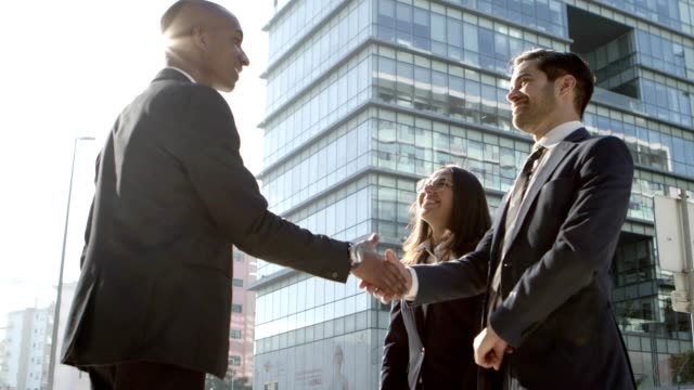 Cheerful business people shaking hands outdoors. Low angle view of multiethnic young business colleagues greeting each other and shaking hands on street. Business meeting concept